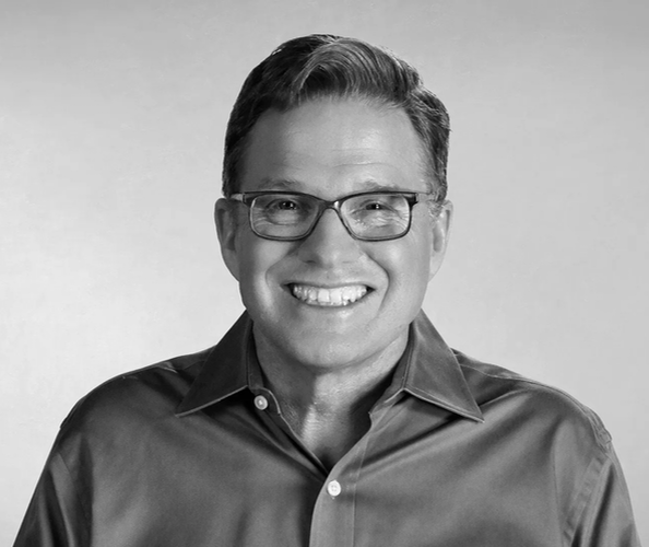 Smiling man in glasses with a gray background.